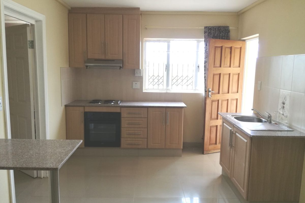 A functional kitchen featuring light wood cabinetry, built-in oven and hob, tiled flooring, and a stainless steel sink with a window view.