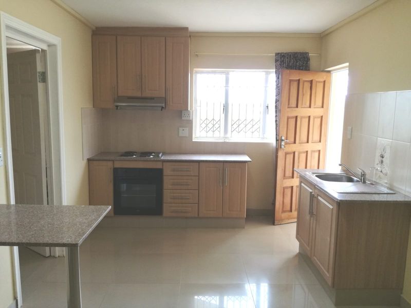 A functional kitchen featuring light wood cabinetry, built-in oven and hob, tiled flooring, and a stainless steel sink with a window view.