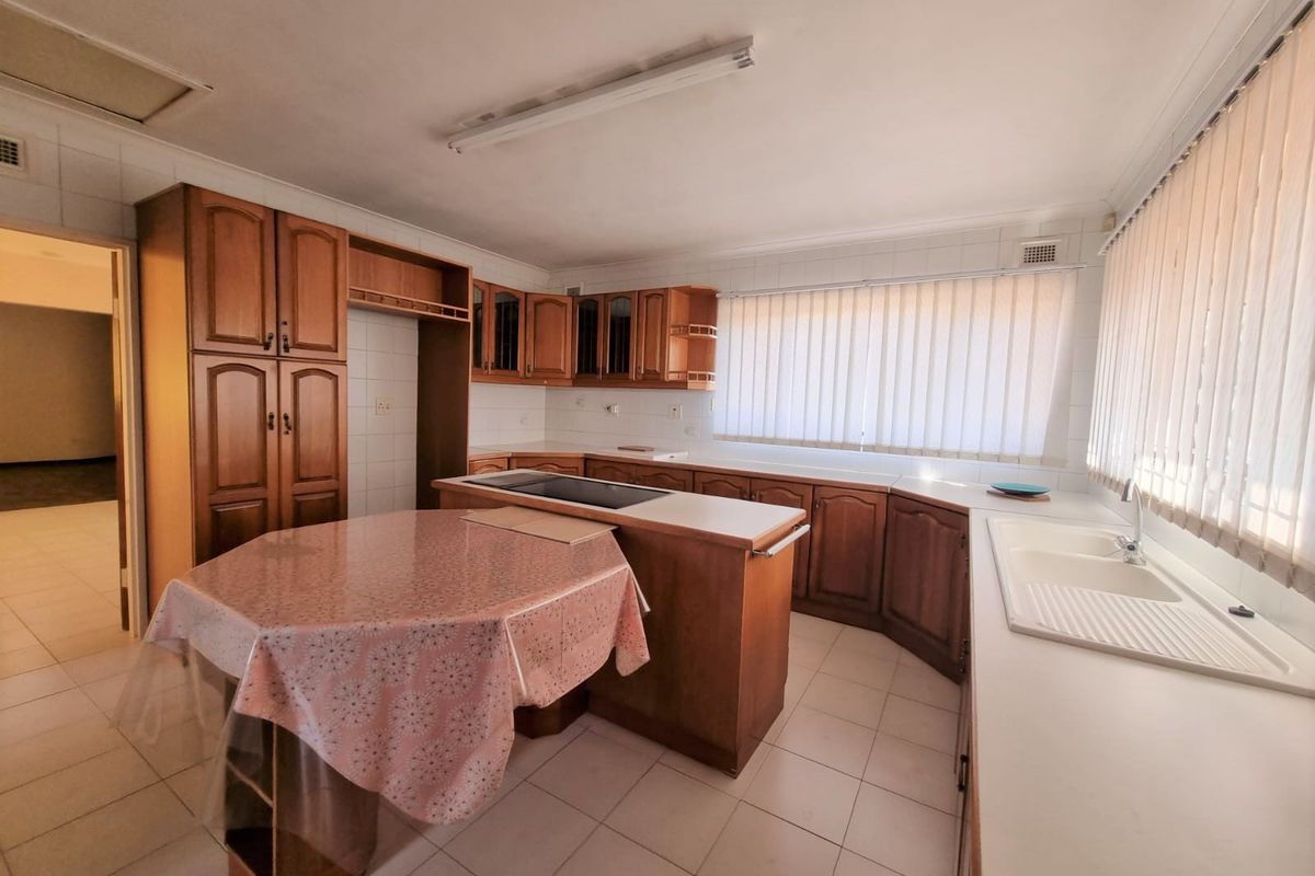 Spacious kitchen featuring traditional timber cabinetry, a central island with integrated cooktop, double sink, and tiled flooring throughout.