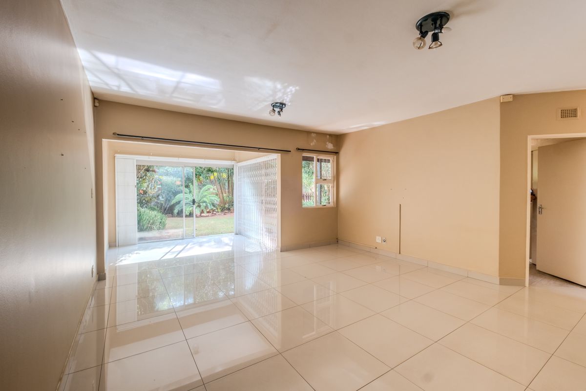 A spacious, empty living room featuring polished tile flooring, neutral walls, and a sliding glass door providing access to the garden.