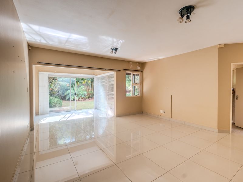 A spacious, empty living room featuring polished tile flooring, neutral walls, and a sliding glass door providing access to the garden.