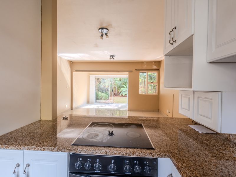 Open plan kitchen and living area featuring granite countertops, electric hob, and direct access to a rear garden through sliding glass doors.
