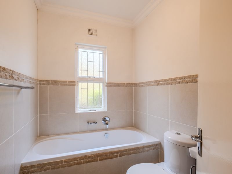 A clean, neutral-toned bathroom featuring a built-in bathtub, toilet, and decorative stone tile accents, providing a functional and well-maintained space.