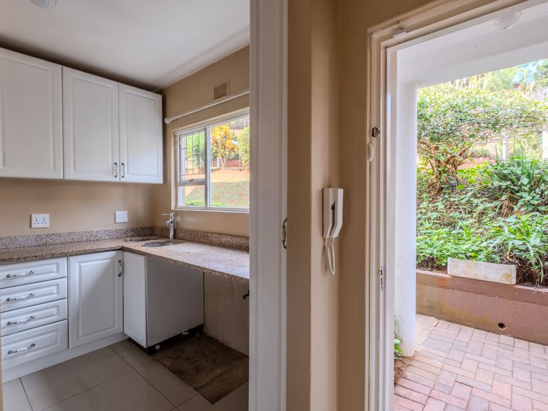 A functional scullery area featuring white cabinetry, granite countertops, a sink, and direct access to an outdoor patio space.