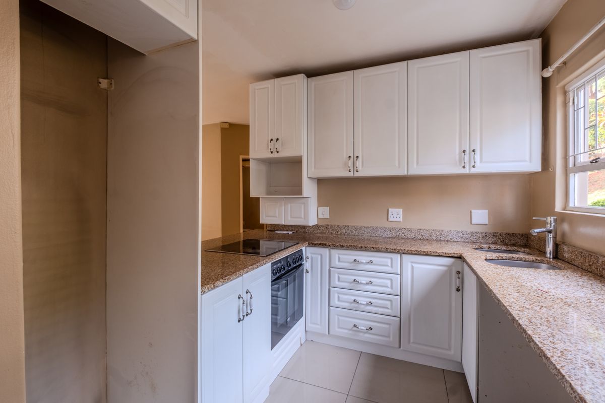 A functional kitchen featuring white cabinetry, granite countertops, a built-in oven, electric hob, and a double sink with a mixer tap.