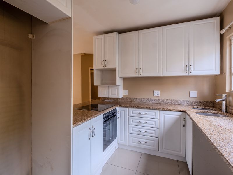A functional kitchen featuring white cabinetry, granite countertops, a built-in oven, electric hob, and a double sink with a mixer tap.