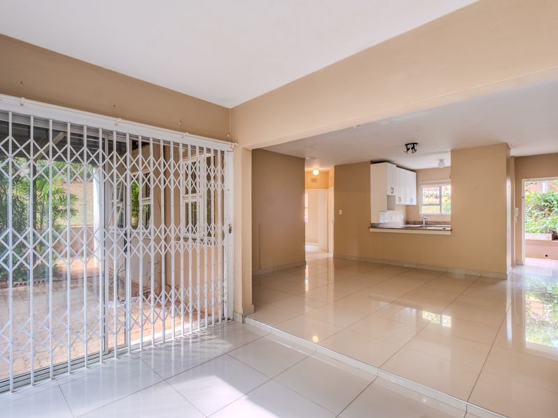 Spacious open-plan living area featuring polished porcelain tiles, a sliding door with security gate, and an integrated kitchen with built-in cabinetry.