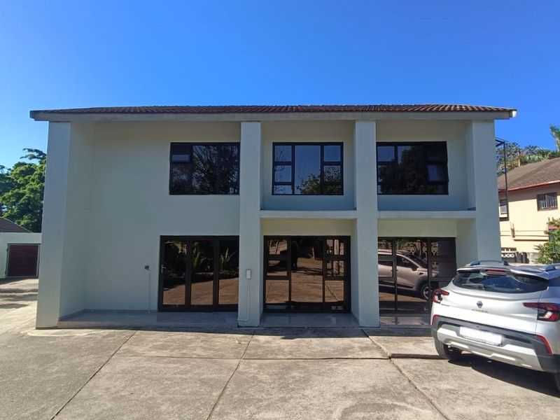 Front elevation of a two-story flat building featuring a concrete driveway, dark-tinted aluminium windows, and sliding glass door access.