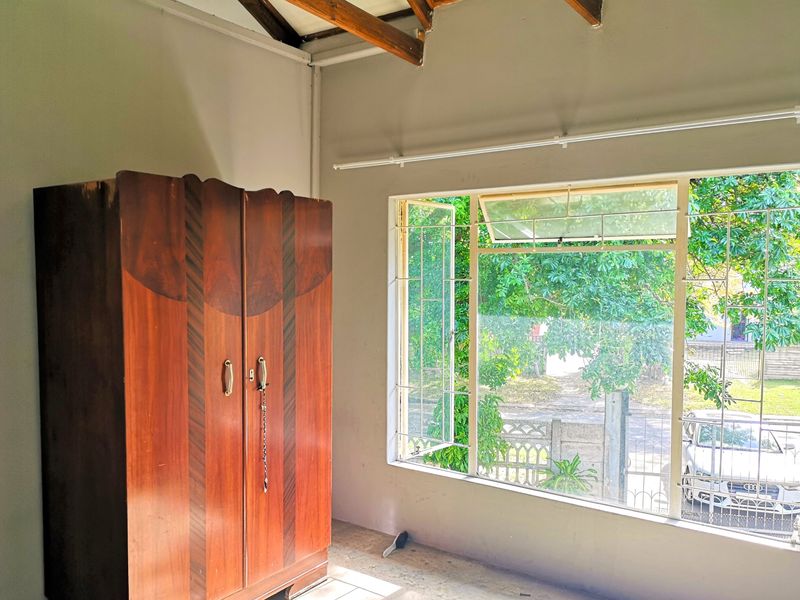 A bedroom featuring exposed timber rafters, large casement windows with security bars, and views of the street.