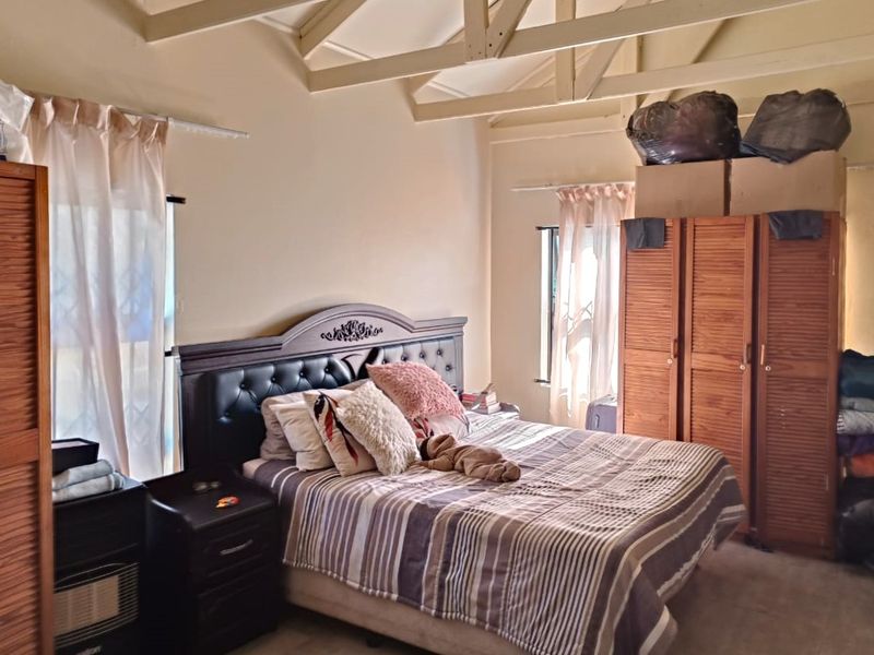 A bedroom featuring a vaulted ceiling with exposed timber rafters and natural light from dual windows.