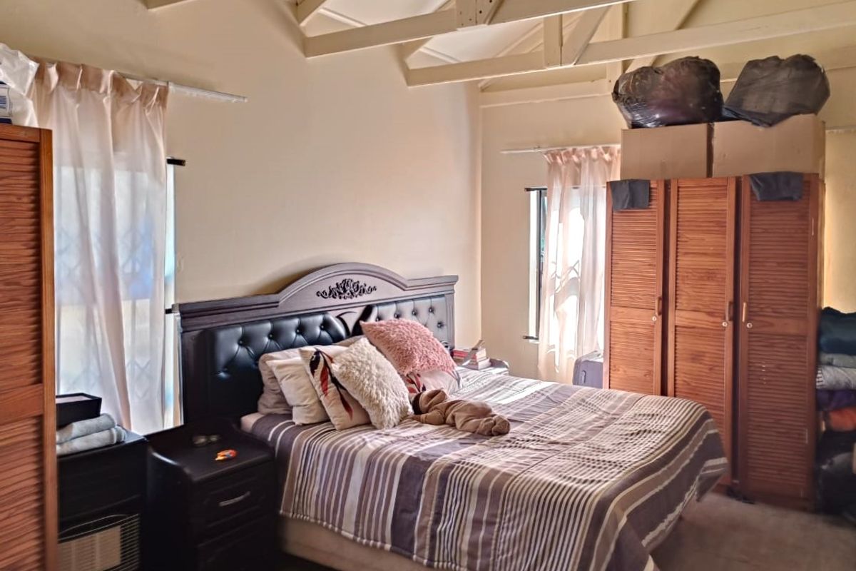 A bedroom featuring a vaulted ceiling with exposed timber rafters and natural light from dual windows.