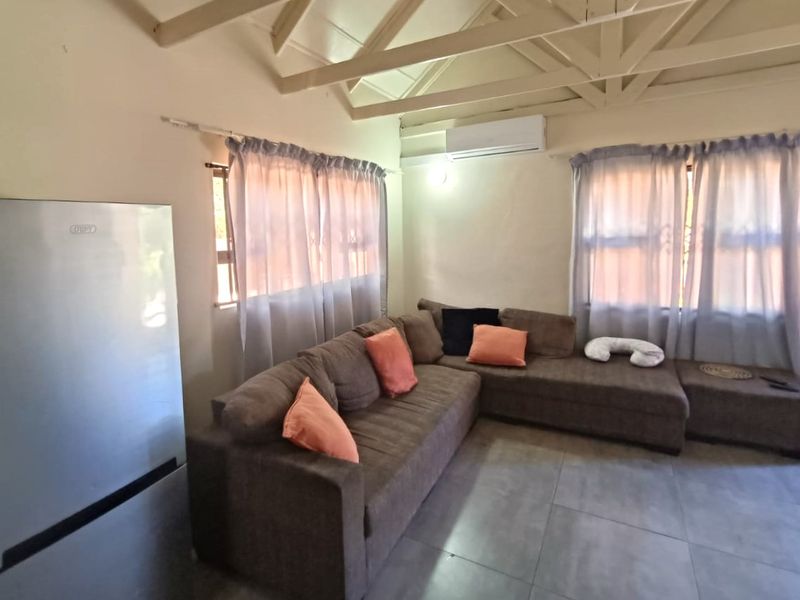 A living room featuring exposed timber ceiling beams, tiled flooring, and a wall-mounted split-system air conditioner.