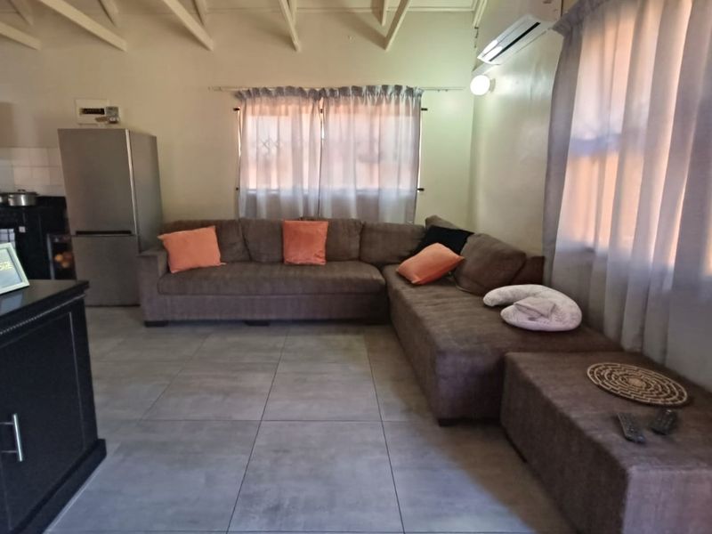 Open-plan living area featuring tiled flooring, exposed rafters, and a wall-mounted air conditioning unit, seamlessly connecting to the kitchen space.
