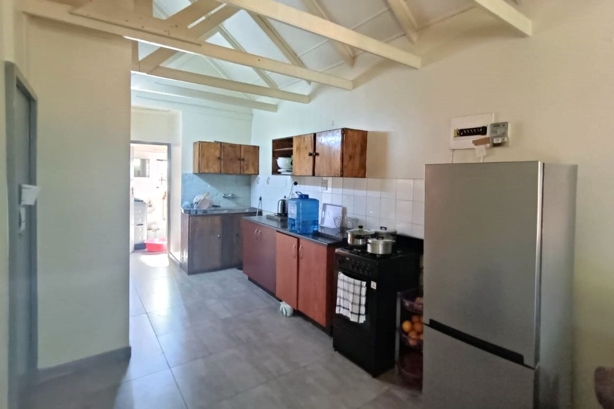 Functional kitchen featuring tiled flooring, built-in cabinetry, a tiled backsplash, and exposed timber roof trusses, leading through to a secondary utility area.