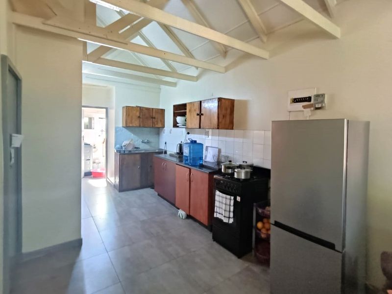 Functional kitchen featuring tiled flooring, built-in cabinetry, a tiled backsplash, and exposed timber roof trusses, leading through to a secondary utility area.