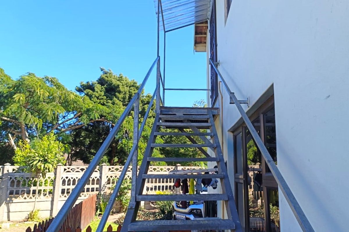 Exterior view of the rear of the property featuring a metal staircase with a polycarbonate canopy and a precast concrete boundary wall.