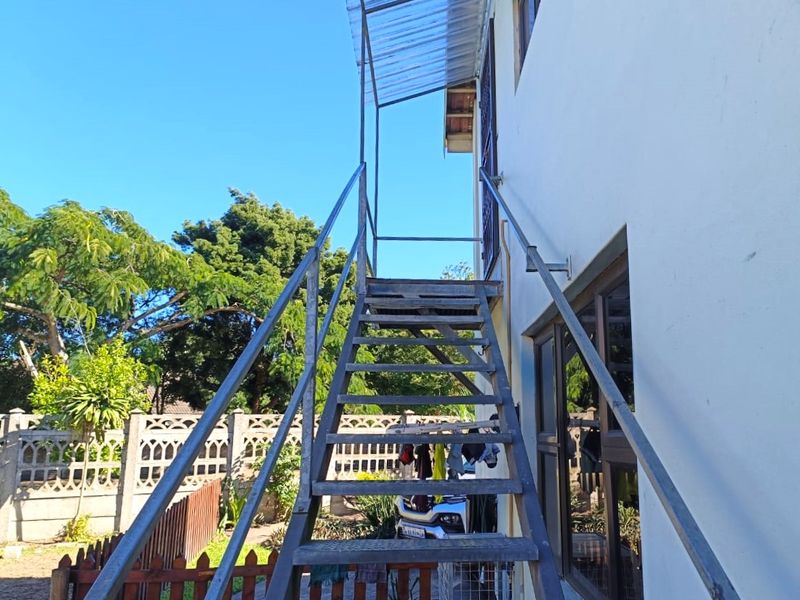 Exterior view of the rear of the property featuring a metal staircase with a polycarbonate canopy and a precast concrete boundary wall.