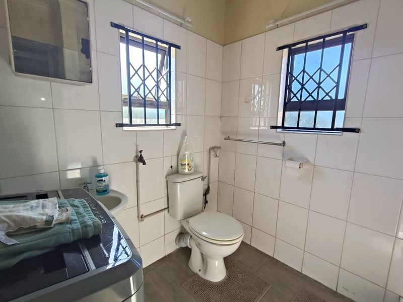 A functional laundry room featuring tiled walls, a toilet, a wash basin, and security bars on the windows.