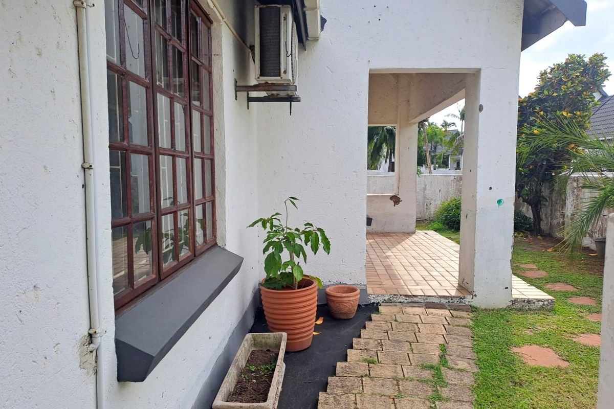 Rear exterior view of the townhouse featuring a covered tiled patio, paved walkway, and wall-mounted air conditioning unit.