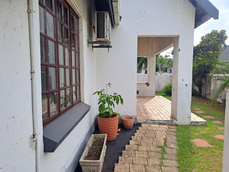 Rear exterior view of the townhouse featuring a covered tiled patio, paved walkway, and wall-mounted air conditioning unit.