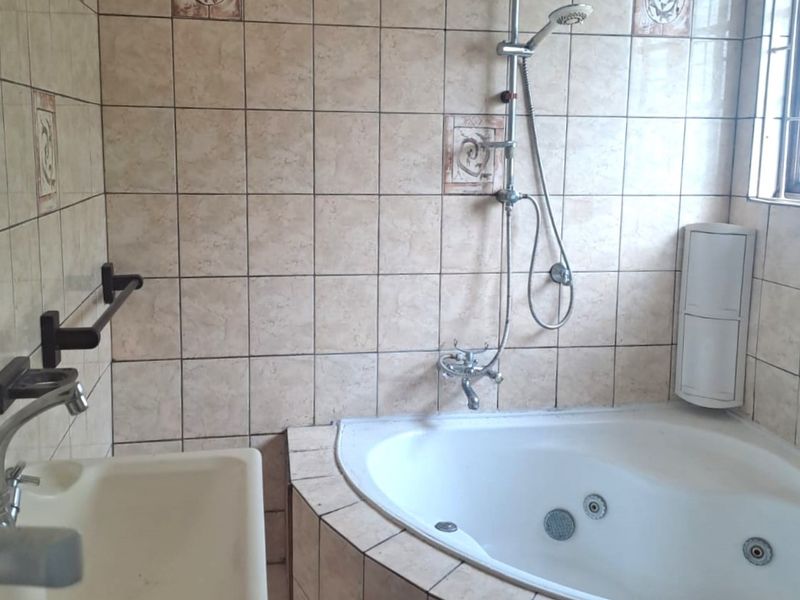A dated bathroom featuring a corner spa bath with integrated shower, wall-mounted basin, and full-height wall tiling.