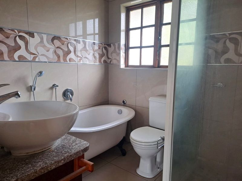 A functional bathroom featuring a freestanding bathtub, vessel sink on a granite vanity, toilet, and a separate shower enclosure with tiled finishes.