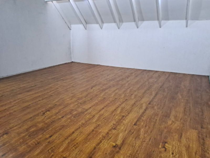 An empty bedroom featuring laminate flooring and exposed rafters, offering a blank canvas for personalization.