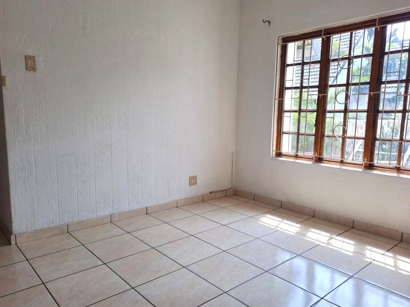An empty bedroom featuring tiled flooring, textured walls, and a wooden window frame with integrated security burglar bars.