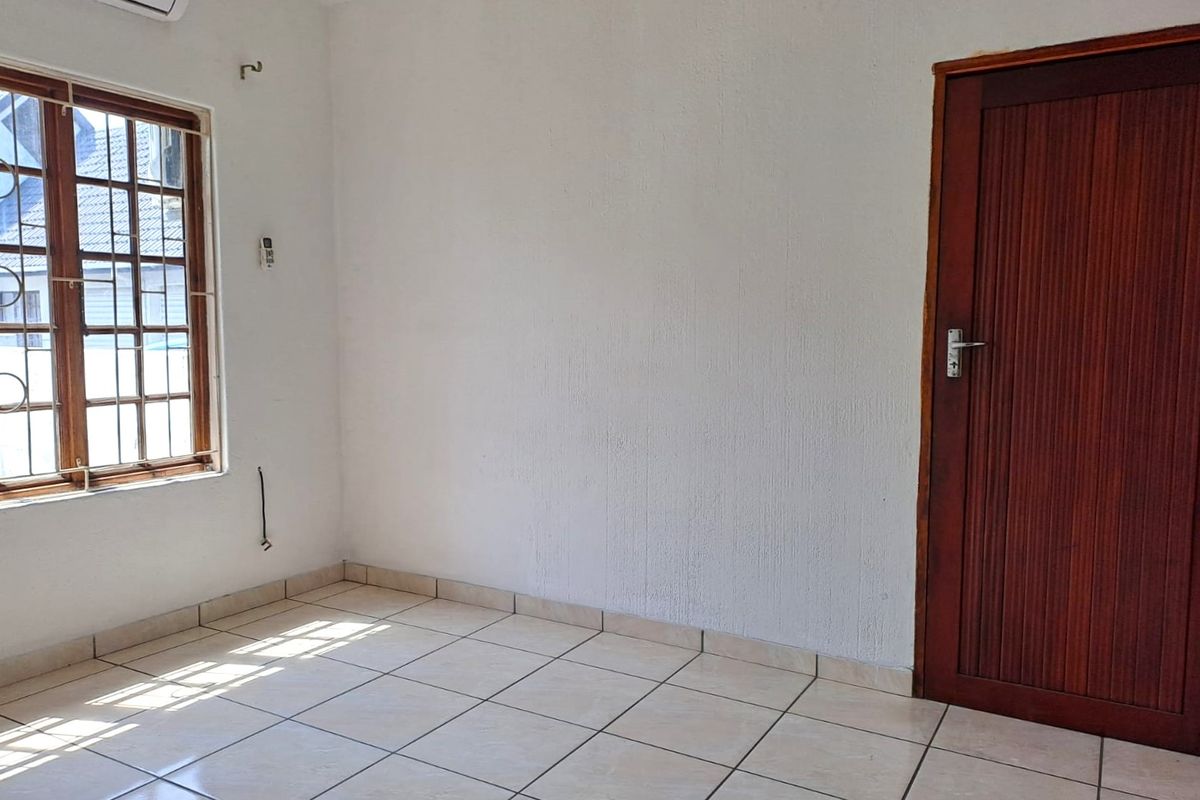 A vacant bedroom featuring tiled flooring, a wooden door, and an installed air conditioning unit, offering a clean canvas for personalization.