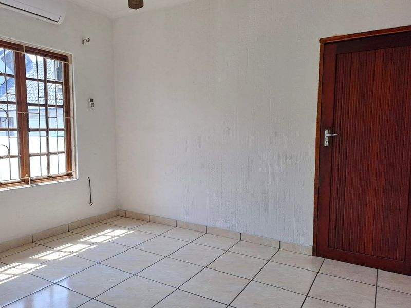 A vacant bedroom featuring tiled flooring, a wooden door, and an installed air conditioning unit, offering a clean canvas for personalization.