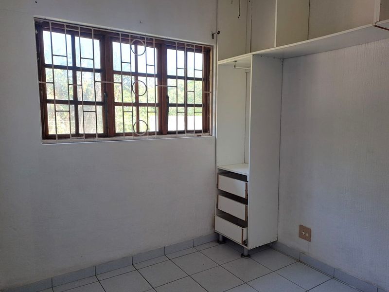 A vacant bedroom featuring tiled flooring, security bars on the window, and a built-in wardrobe with missing drawer fronts.