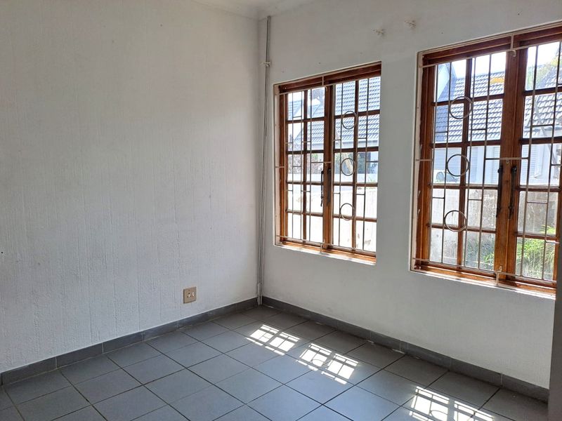 An empty bedroom featuring tiled flooring and wooden-framed windows with security bars, offering a blank canvas for potential interior design updates.