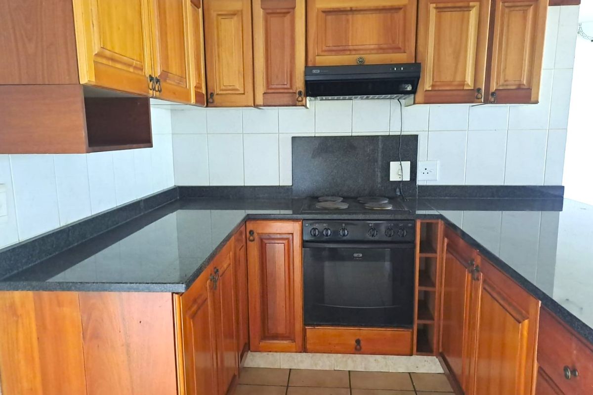 A functional kitchen featuring wooden cabinetry, granite countertops, a built-in oven, and an electric hob with an extractor fan.