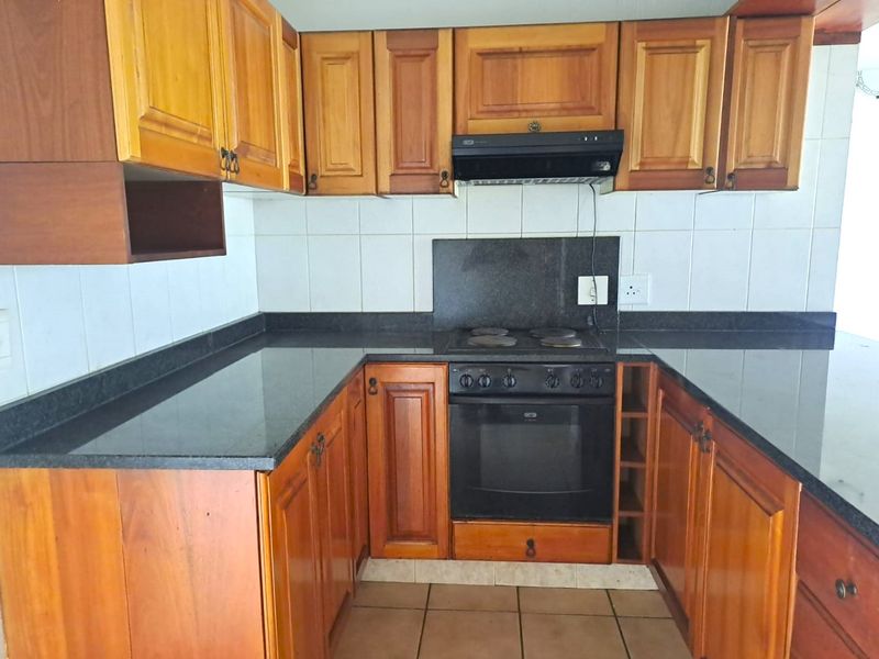 A functional kitchen featuring wooden cabinetry, granite countertops, a built-in oven, and an electric hob with an extractor fan.