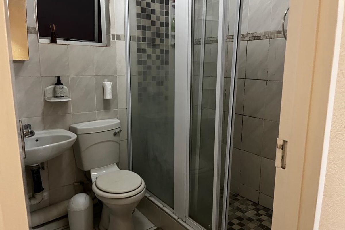 A functional bathroom featuring a shower enclosure, pedestal basin, and toilet with tiled finishes throughout.