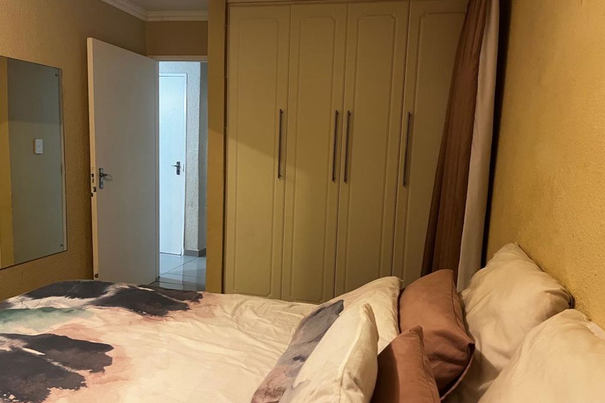 A bedroom featuring built-in cupboards with vertical handles and a wall-mounted mirror, providing functional storage and a neutral aesthetic.