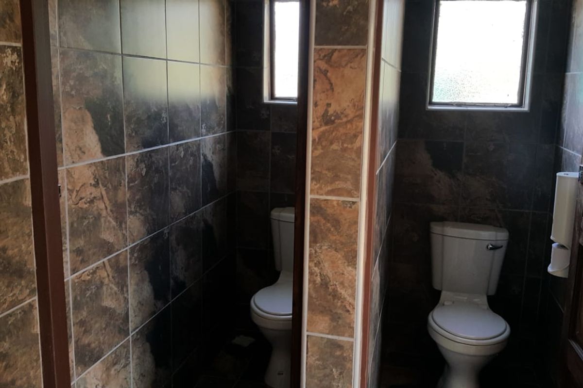 A functional bathroom space featuring dual toilet cubicles with dark stone-look ceramic wall tiling and natural light from small casement windows.