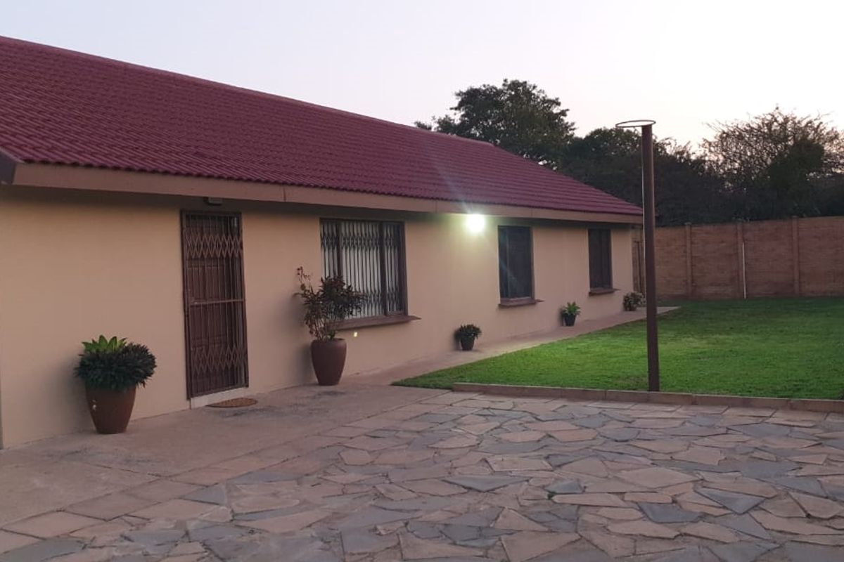 Rear view of the farm property featuring a paved patio area, well-maintained lawn, and secure building exterior with tiled roofing.