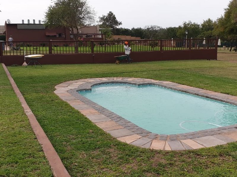 A well-maintained outdoor pool area featuring stone coping, surrounded by a spacious lawn and secure perimeter fencing on the farm property.