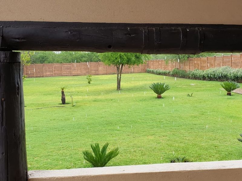 A view from a covered patio looking out over a spacious, well-maintained green lawn and garden area.