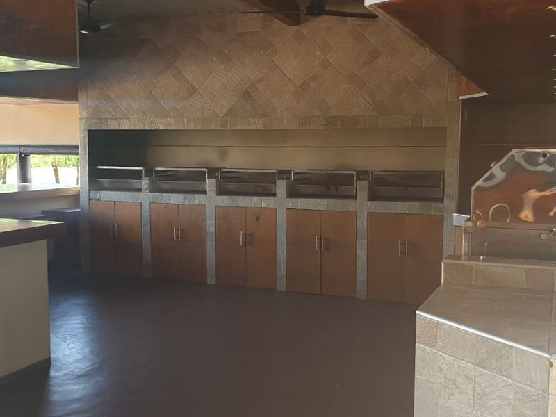 Spacious covered outdoor entertainment area featuring a large built-in braai, tiled prep surfaces, and wooden cabinetry, ideal for hosting gatherings.