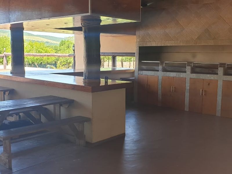 Spacious covered outdoor entertainment area featuring a built-in braai, bar counter, and wooden cabinetry, overlooking the surrounding farm landscape.