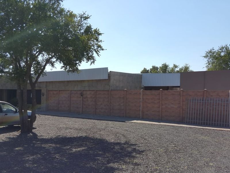 Front exterior view of the farm property featuring a gravel driveway, perimeter precast concrete walling, and metal roof structure.