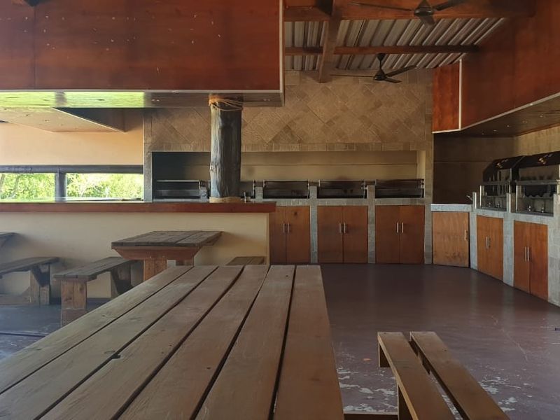 Spacious covered outdoor entertainment area featuring a large built-in braai, extensive wooden cabinetry, and exposed timber ceiling beams.