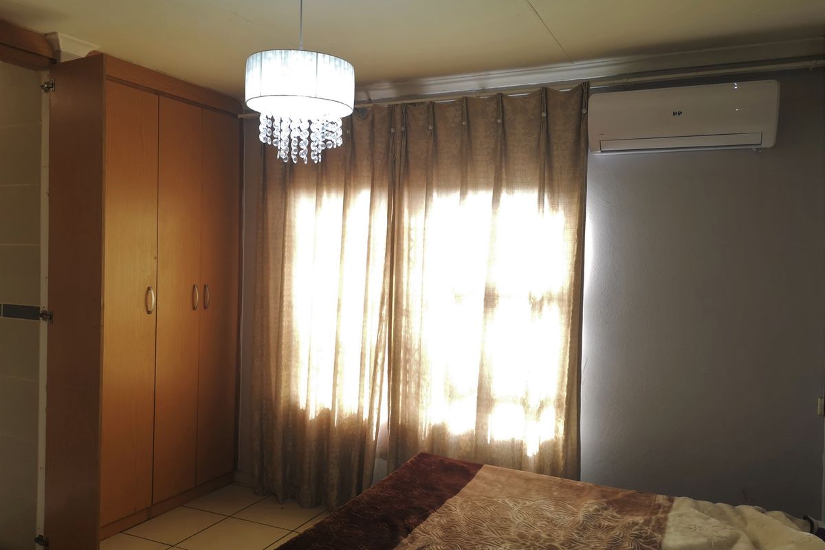 A bedroom featuring built-in wooden cupboards, tiled flooring, and a wall-mounted air conditioning unit.