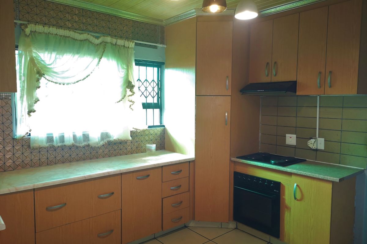 A functional kitchen featuring wood-look cabinetry, built-in oven and hob, tiled flooring, and a window with security bars.