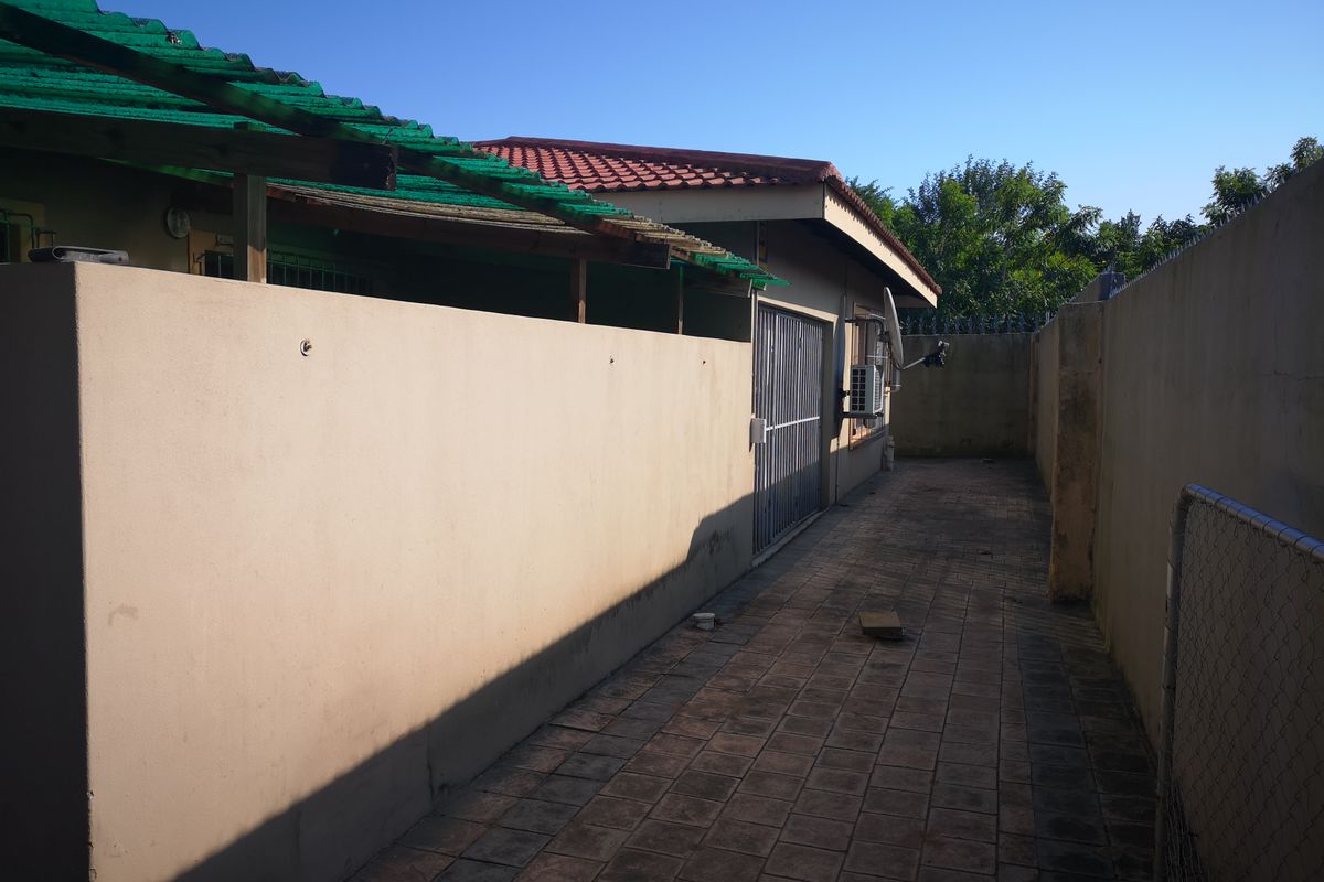 A paved side walkway along the exterior of the property, featuring boundary walls with security spikes and an external air conditioning unit.