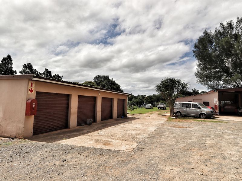 Exterior view of a commercial office property featuring multiple roller shutter garage doors, a concrete driveway, and a covered parking area.