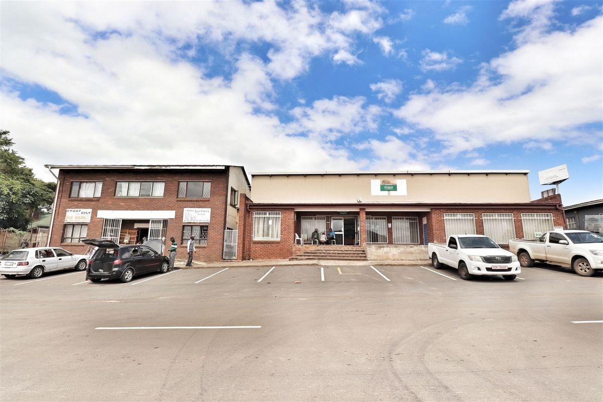 Front exterior view of a commercial office building featuring a brick facade, paved parking area, and multiple ground-level entrances.