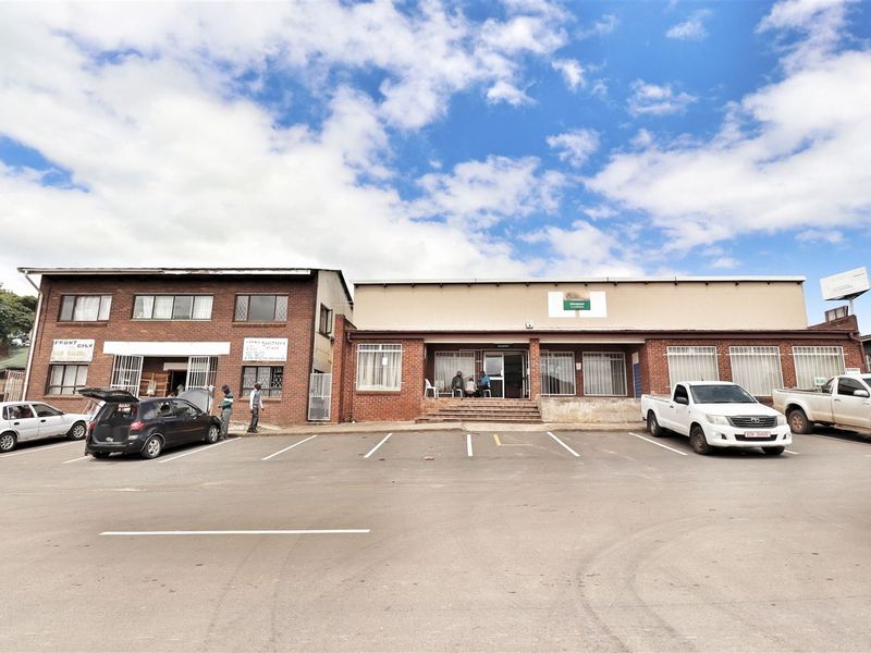Front exterior view of a commercial office building featuring a brick facade, paved parking area, and multiple ground-level entrances.